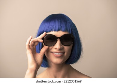 Portrait Of Beautiful And Sexy Woman With Blue Wig And Sunglasses Looking To Camera With Smile. Sun Tan, Pink Lipstick And White Teeth. Model With Naked Shoulders. Toned Image With Brown Color