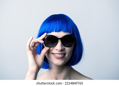 Portrait Of Beautiful And Sexy Woman With Blue Wig And Sunglasses Looking To Camera With Smile. Sun Tan, Pink Lipstick And White Teeth. Model With Naked Shoulders. Toned Image With Blue Color