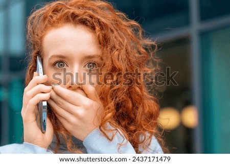 Portrait of beautiful shocked young redhead woman with a gaze talking on the mobile closing her mouth as she getting terrible news