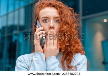 Portrait of beautiful shocked young woman with curly red hair talking on the mobile as she getting terrible news