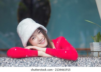 Portrait beautiful skin of Asian woman who wears red long sleeve cardigan and a cream hat smiles happily and looking at camera.