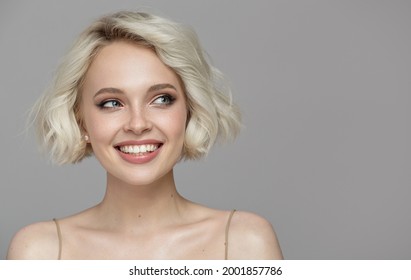 Portrait of a beautiful smiling blonde girl with a short haircut. Gray background.