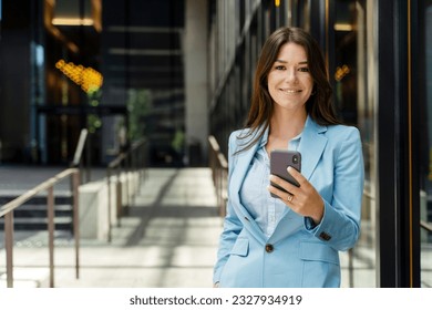 Portrait of beautiful smiling businesswoman wearing formal wear, business suit, holding phone, texting message, looking at camera, copy space. Attractive female online shopping, mobile banking