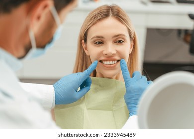 Portrait of beautiful smiling caucasian woman looking in mirror, checking her teeth in modern mental clinic. Health care concept  - Powered by Shutterstock