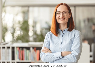 Portrait of beautiful smiling confident businesswoman, manager, CEO holding arms crossed looking at camera. Happy smart university student wearing eyeglasses standing in modern library, education - Powered by Shutterstock