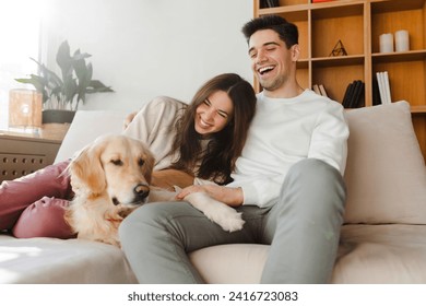 Portrait of beautiful, smiling couple, attractive man and woman petting golden retriever while sitting on comfortable sofa in cozy home. Concept of love, pet care - Powered by Shutterstock