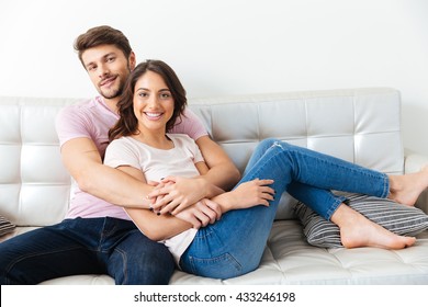 Portrait Of A Beautiful Smiling Couple Sitting On The Sofa Isolated On White Background