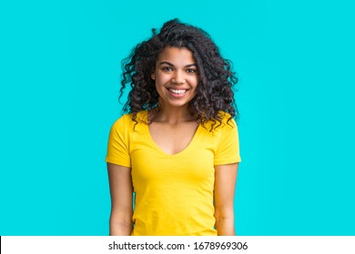Portrait of beautiful smiling dark skinned girl wearing bright colored yellow t-shirt isolated over blue background.