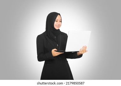 Portrait Of Beautiful Smiling Hijab Asian Business Woman Carrying Laptop While Standing Isolated On Gray Background