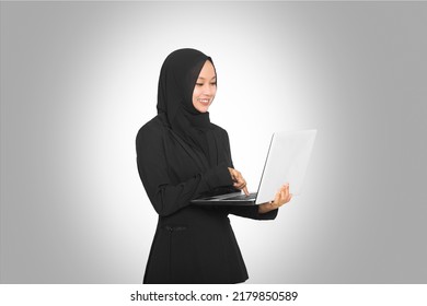 Portrait Of Beautiful Smiling Hijab Asian Business Woman Carrying Laptop While Standing Isolated On Gray Background