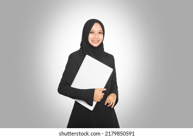 Portrait Of Beautiful Smiling Hijab Asian Business Woman Carrying Laptop While Standing Isolated On Gray Background