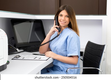 Portrait Of A Beautiful Smiling Nurse At Desk Station While Talking On The Phone And Complete A Medical Information Form