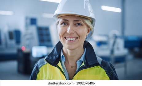 Portrait of Beautiful Smiling on Camera Female Engineer in Safety Vest and Hardhat. Professional Woman Working in the Modern Manufacturing Factory. Facility with CNC Machinery Robot arm
