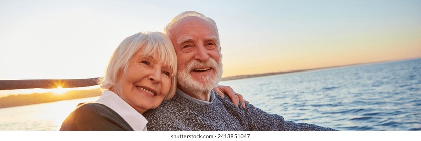 Portrait of beautiful smiling senior couple holding hands, hugging and relaxing together while sitting on the side of sailboat or yacht floating in sea on a sunny day - Powered by Shutterstock