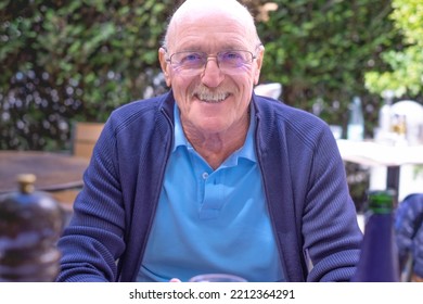 Portrait Of Beautiful Smiling Senior Man With Moustache And Eyeglasses Sitting In Outdoor. Elderly Caucasian Male Looking At Camera