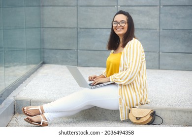 Portrait Of Beautiful And Smiling Stylish Plus Size Business Woman 30-35 Years Old In Yellow Fashion Clothes And Eyeglasses, Working Remotely On A Laptop On Vacation. 