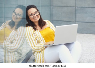 Portrait Of Beautiful And Smiling Stylish Plus Size Business Woman 30-35 Years Old In Yellow Fashion Clothes And Eyeglasses, Working Remotely On A Laptop On Vacation. 