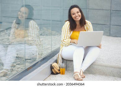 Portrait Of Beautiful And Smiling Stylish Plus Size Business Woman 30-35 Years Old In Yellow Fashion Clothes And Eyeglasses, Working Remotely On A Laptop On Vacation. 