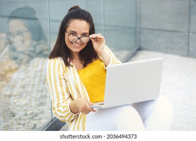 Portrait Of Beautiful And Smiling Stylish Plus Size Business Woman 30-35 Years Old In Yellow Fashion Clothes And Eyeglasses, Working Remotely On A Laptop On Vacation. 