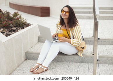 Portrait Of Beautiful And Smiling Stylish Plus Size Business Woman 30-35 Years Old In Yellow Fashion Clothes And Sunglasses, Working Remotely On A Laptop On Vacation. 