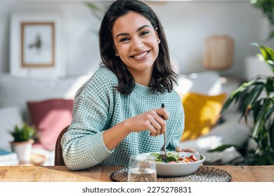 Portrait of beautiful smiling woman eating healthy salad while looking at camera at home. - Powered by Shutterstock