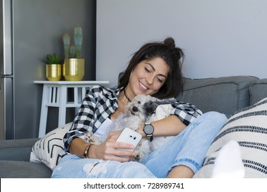 Portrait of beautiful  smiling woman hugging her dog and using mobile phone at home