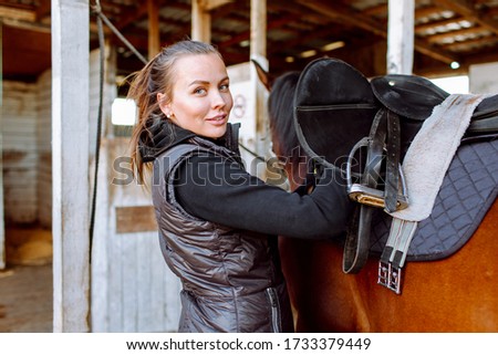 Portrait beautiful smiling woman long hair next to her horse in a stable. Horseback riding