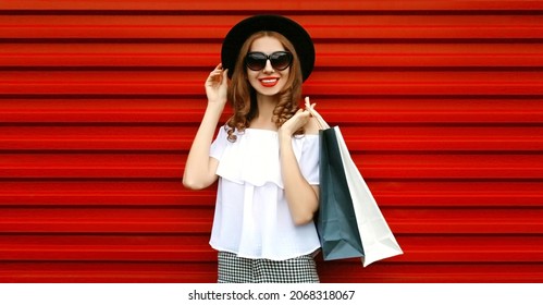 Portrait of beautiful smiling woman with shopping bags wearing black round hat on red background - Shutterstock ID 2068318067