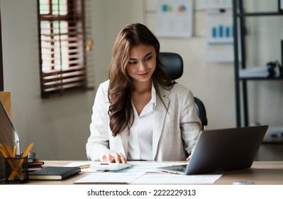 Portrait of beautiful smiling young brunette businesswoman sitting at bright modern work office and typing on laptop - Shutterstock ID 2222229313