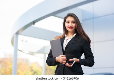Portrait of a beautiful smiling young business woman with cell phone (mobile). Modern building as background.