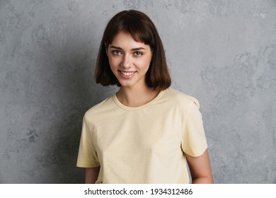 Portrait of a beautiful smiling young girl in casual clothes standing isolated over gray background, looking at camera