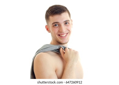 Portrait of a beautiful smiling young guy who looks into the camera and keeps the shoulder t-shirt close-up