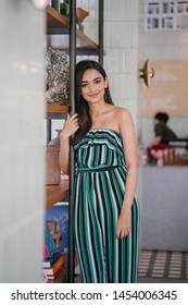 Portrait Of A Beautiful, Sophisticated And Attractive Young Indian Asian Woman (high Society) In An Elegant Green Outfit Smiling As She Stands Next To A Bookshelf In Her Well-appointed Home.