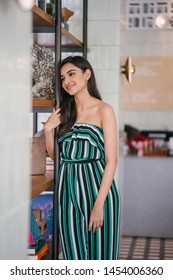 Portrait Of A Beautiful, Sophisticated And Attractive Young Indian Asian Woman (high Society) In An Elegant Green Outfit Smiling As She Stands Next To A Bookshelf In Her Well-appointed Home.