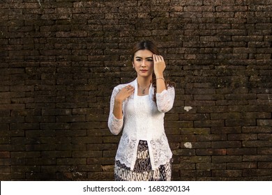 Portrait Of Beautiful South East Asian Woman Wearing Jewelry And White Traditional Cloth With Brick Wall Background.Calm Face Expression Medium Close Up Photography,