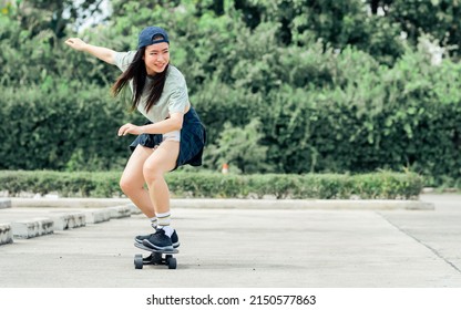 Portrait beautiful sportive Asian female skater wearing hipster shirt with shorts, smiling with happiness, standing on skateboard and playing outdoor with copy space. Activity and Adventure Concept