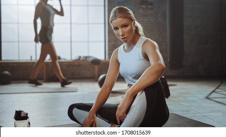 Portrait of a Beautiful Strong Fit Blond Sitting in a Loft Industrial Gym with Motivational Posters. She's Catching Her Breath after Intense Fitness Training Program. - Powered by Shutterstock