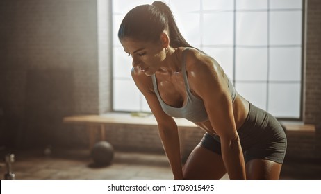 Portrait of a Beautiful Strong Fit Brunette Wiping Sweat from Her Face in a Loft Industrial Gym with Motivational Posters. She's Catching Her Breath after Intense Fitness Training Workout. Warm Light. - Powered by Shutterstock