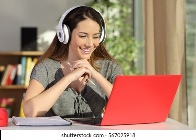 Portrait of a beautiful student viewing and listening video tutorials on line with headphones and a red pc sitting in a table at home - Powered by Shutterstock