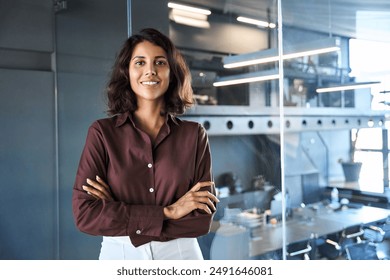 Portrait of beautiful successful hispanic young business woman with crossed arms smiling confident at camera. Latin or eastern middle age female ceo leader businesswoman standing in office. Copy space