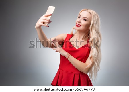 Portrait of a Beautiful successful smiling girl doing selfie in  red dress on  light background