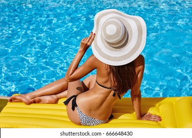 Portrait Of Beautiful Tanned Woman Relaxing In Bikini And Hat In Swimming Pool. Gel Polish Red Manicure And Pedicure. Hot Summer Day And Bright Sunny Light.