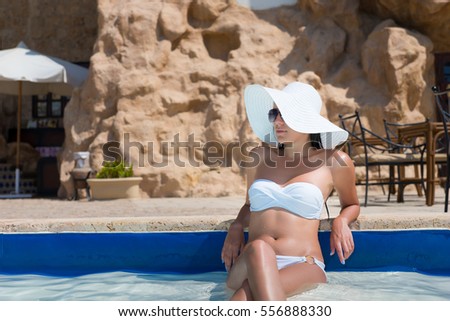 Portrait of beautiful tanned woman relaxing in swimming pool spa wearing white hat and white bikini