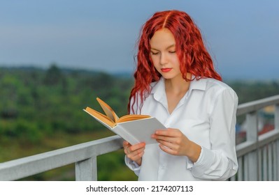 Portrait of beautiful teen girl reading the book at balcony