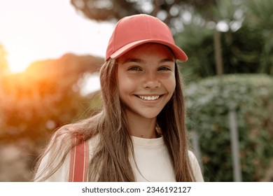 Portrait of beautiful teenage girl (14-15 years old) wearing a pink baseball cap, stands outdoors, sweetly smiling against the backdrop of a sunset. - Powered by Shutterstock