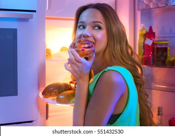 Portrait Of Beautiful Teenage Girl Taking Food From Refrigerator At Night. Night Eating, Overeat Concept. Diet, Dieting. Beauty Young Woman Eating Pastries In Fridge At Night Kitchen.