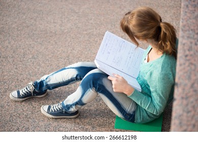 Portrait Of A Beautiful Teenage Student Girl Sitting On Stairs In Park With Copy Book And Studing. Sunny Summer Day. Modern And Casual Lifestyle. Woman With Note Pad.