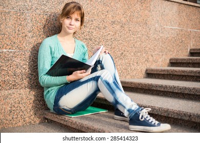 Portrait Of A Beautiful Teenage Student Girl Sitting On Stairs In Park With Copy Book And Studing. Sunny Summer Day. Modern And Casual Lifestyle. Woman With Note Pad.