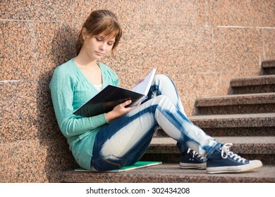 Portrait Of A Beautiful Teenage Student Girl Sitting On Stairs In Park With Copy Book And Studing. Sunny Summer Day. Modern And Casual Lifestyle. Woman With Note Pad.