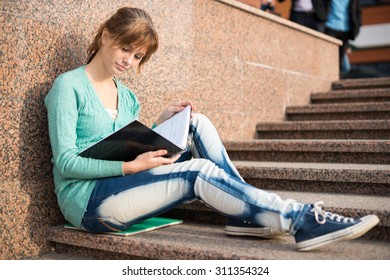 Portrait Of A Beautiful Teenage Student Girl Sitting On Stairs In Park With Copy Book And Studing. Sunny Summer Day. Modern And Casual Lifestyle. Woman With Note Pad.